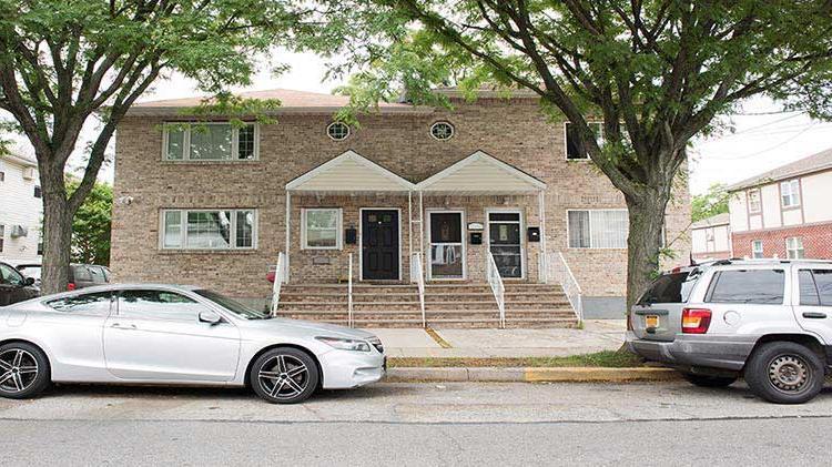 A white car is parked on the street in front of an apartment entrance.